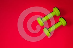 Green dumbbells isolated on a red background. Flatlay concept of fitness, gym and healthy lifestyle. The view from the top and