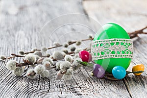 Green Easter egg decorated with lace and willow branch on wooden background. Selective focus