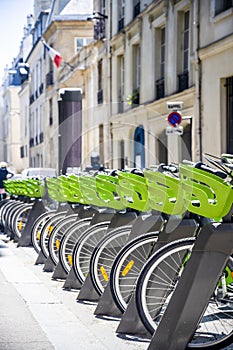 Green electric bicycles with baskets for public rental await cycling tourists on the streets of old Paris