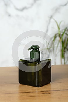 Green empty plastic cosmetic bottle with pump on table in bathroom. Square beauty product packaging for hand wash soap