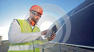 Green energy concept. Engineer is working with his tablet computer and glancing at a solar battery