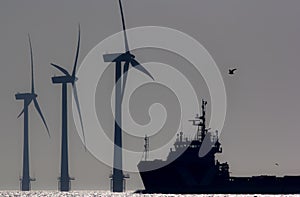 Green energy. Offshore wind farm turbines with ship at sea. Silhouette at dawn.