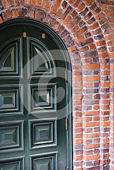 Green entrance arched door framed by brick arch of the building