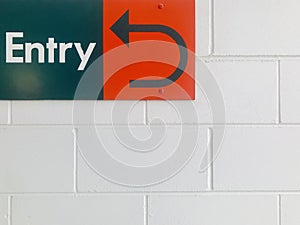 A green Entry sign with a red arrow indicates on white brick wall.