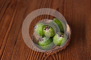 Green feijoa in a coconut shell hulf on a wooden background. Ripe tropical fruits, raw vegan food.Vitamin C. Copy space