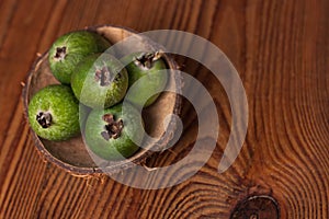 Green feijoa in a coconut shell hulf on a wooden background. Ripe tropical fruits, raw vegan food.Vitamin C. Copy space.