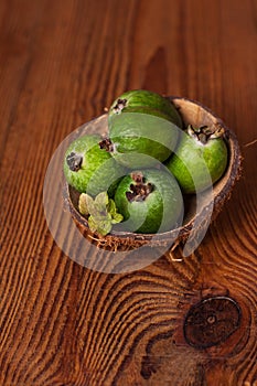 Green feijoa in a coconut shell hulf on a wooden background. Ripe tropical fruits, raw vegan food.Vitamin C. Copy space