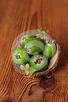 Green feijoa in a coconut shell hulf on a wooden background. Ripe tropical fruits, raw vegan food.Vitamin C. Copy space