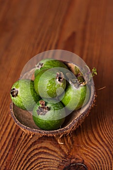 Green feijoa in a coconut shell hulf on a wooden background. Ripe tropical fruits, raw vegan food.Vitamin C. Copy space