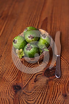 Green feijoa in a coconut shell hulf on a wooden background. Ripe tropical fruits, raw vegan food.Vitamin C. Copy space