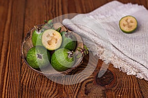 Green feijoa in a coconut shell hulf on a wooden background. Ripe tropical fruits, raw vegan food.Vitamin C. Copy space