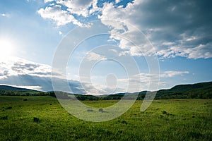 Green field with the cloudy morning sky with hills in the background