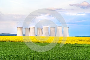 Green field, yellow rapeseed field, cooling towers of nuclear power plant in background