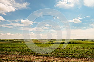 Green fields with ravines to the horizon under a blue cloudy sky