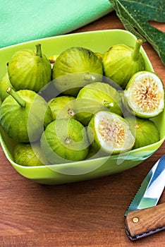 Green figs, fresh and ripe. With a fig leaf Wood background.Whole and cut green, fresh and ripe figs. With fig leaf and knife.