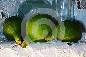 GREEN FIGS ON A SHELF WITH WHITE ANGLAISE CLOTH AND VINTAGE BOTTLES
