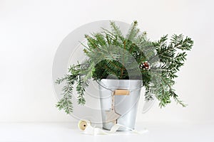 Green fir branches in metalic bucket. Christmas composition with pinecones, wooden star and spool of ribbon lying on