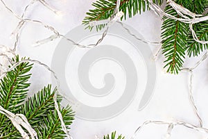 Green fir tree branches and lights on light background with copy space as a Christmas frame. Traditional Xmas and winter holidays