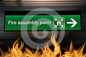 Green fire assembly point sign hanging from ceiling with fire