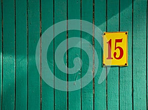Green flaky paint on an old weathered wooden wall with plate number fiveteen. Wood wall with shadows. Peeling paint