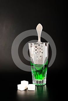 Green flavoured vodka called Absinthe served in a shot glass with a special spoon with white sugar cubes photo