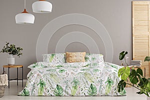 Green flower in vase on nightstand next to king size bed with floral bedding and peach colored pillow, copy space on the empty