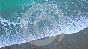 Green foamy ocean waves coming ashore, splashing on sand beach in slow motion