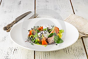 A green French bistro style salad with poached egg and chives on a white plate and table setting photo