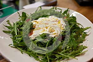 A green French bistro style salad with poached egg and chives on a white plate and table setting. photo