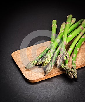 Green fresh asparagus on a wooden board on a black background. Copy space