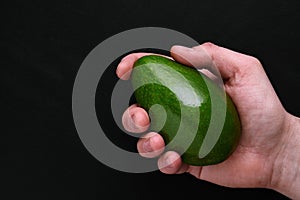 Green fresh avocado in male hand over black background close-up