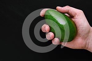 green fresh avocado in male hand over black background close-up