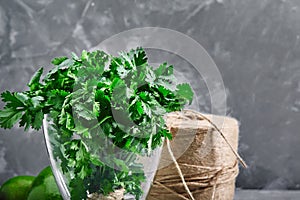 Green fresh bunch of parsley in a glass with water on a gray background. Greens rich in minerals and trace elements