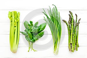 Green fresh herbs and vegetables on white wooden background. Flat lay, eco vegan background