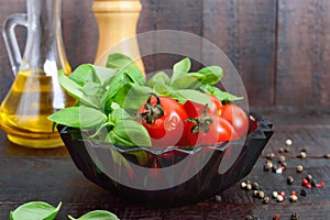 Green fresh leaves of organic basil and small ripe tomatoes, oil and pepper