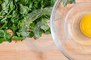 Green fresh parsley preparing to be chopped. Egg in a bowl. Wood cutting board