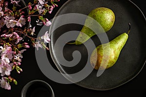 Green fresh pears lie on a black plate, next to spring flowers, top view