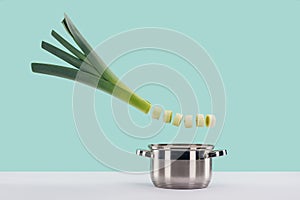 Green fresh sliced leek above saucepan on white surface isolated on turquoise.