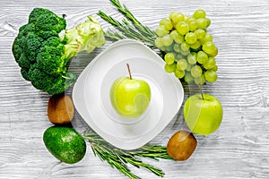green fresh vegetables, fruits and apple on plate for healthy salad gray background top view