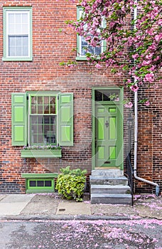 Green front door entrance and old-style window with shutters of a red brick house in spring.