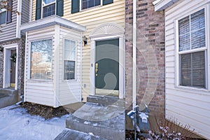 Green front door of a townhouse with vinyl wood and bricks siding