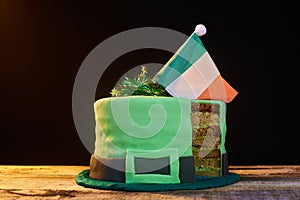 Green frosting cake shaped like a green hat with an Irish flag on top, to celebrate St. Patrick`s Day. Natural wood base