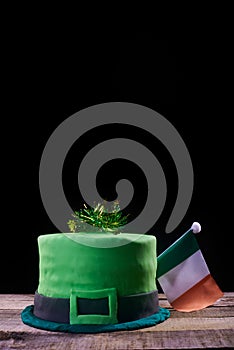 Green frosting cake shaped like a green hat with an Irish flag on top, to celebrate St. Patrick`s Day. Natural wood base