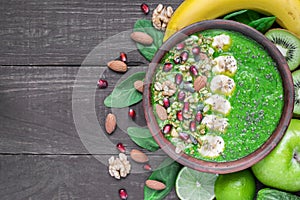 Green fruit and vegetable smoothie bowl topped with granola, banana, pomegranate, pumpkin and chia seeds