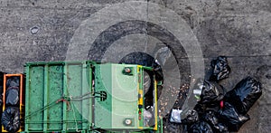 Green garbage truck Collecting a large number of black garbage bags that are tied up On the sidewalk To discard Viewed from the to photo