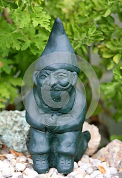 Green garden ornament gnome sitting down on stones