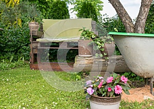 The green garden in summer, homemade wooden chair from pallets for relaxing in the garden, blooming colorful flowers in pots