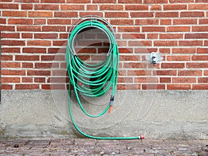 Green Garden Water Hose mounted on Red Brickwall