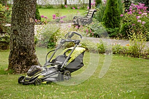 Green gasoline lawn mower in the backyard garden. Plant care and landscape design concept