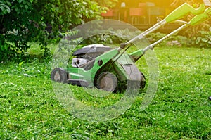 Green gasoline lawn mower on the grass in the park on the lawn